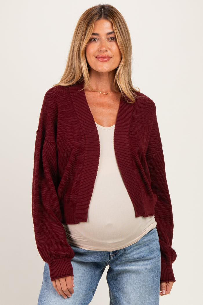woman wearing a burgundy lightweight maternity cardigan over a beige top and showing her baby bump with relaxed fit jeans