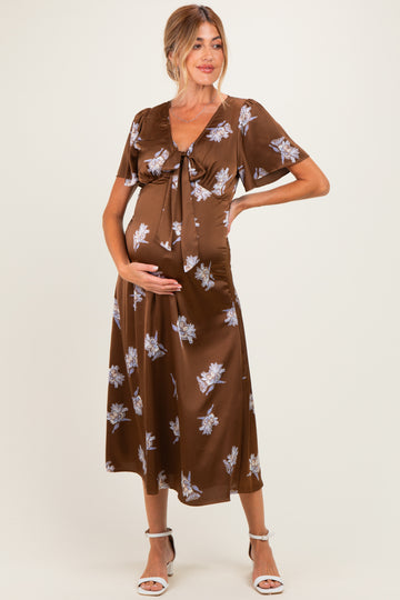 woman wearing a brown floral print maternity dress with short sleeves and a tie front, showing her baby bump