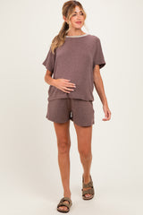 woman wearing a brown maternity loungewear set with a loose top and shorts, holding her baby bump