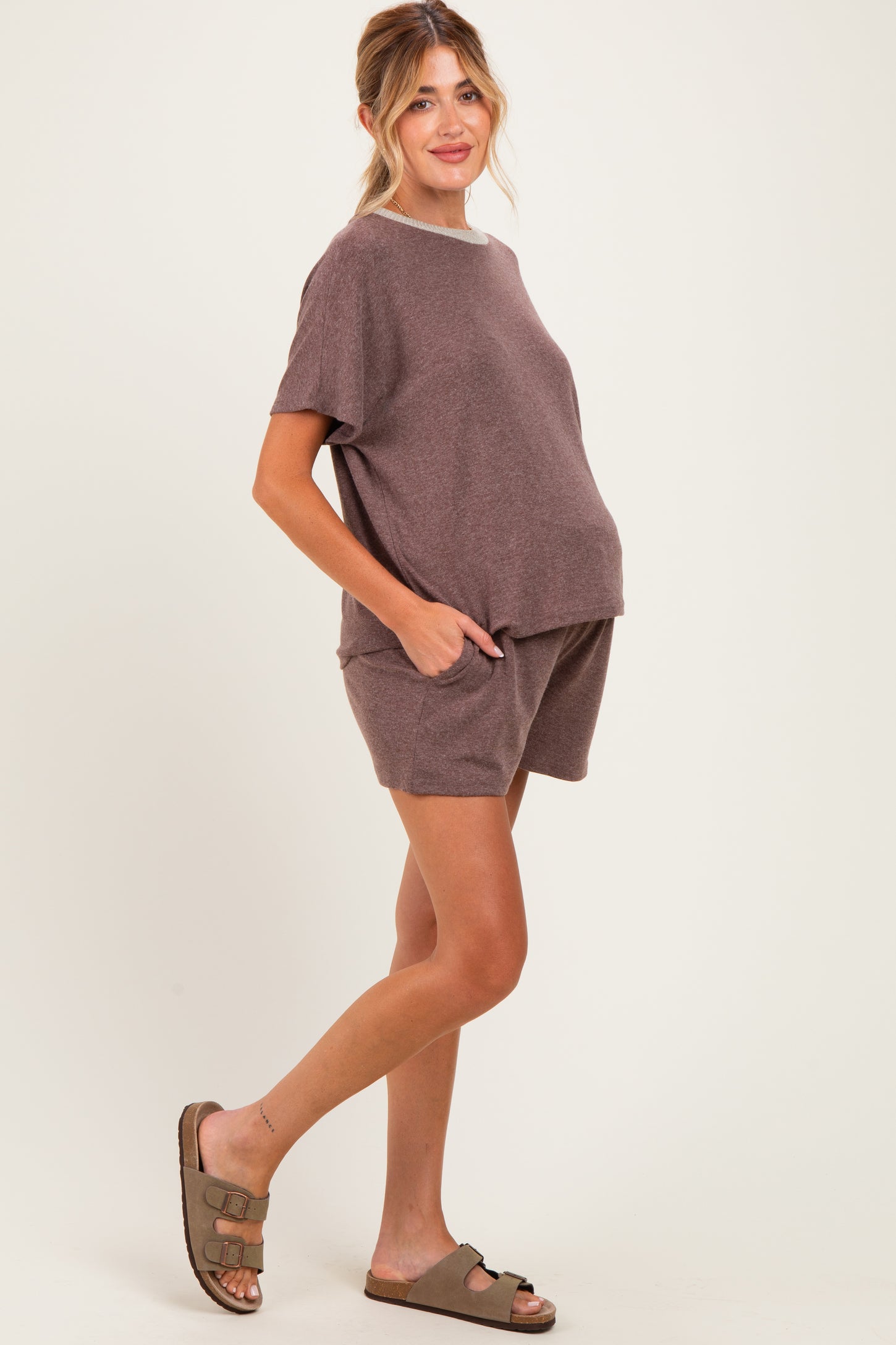 woman wearing a brown short sleeve maternity top and matching shorts, gently cradling her baby bump