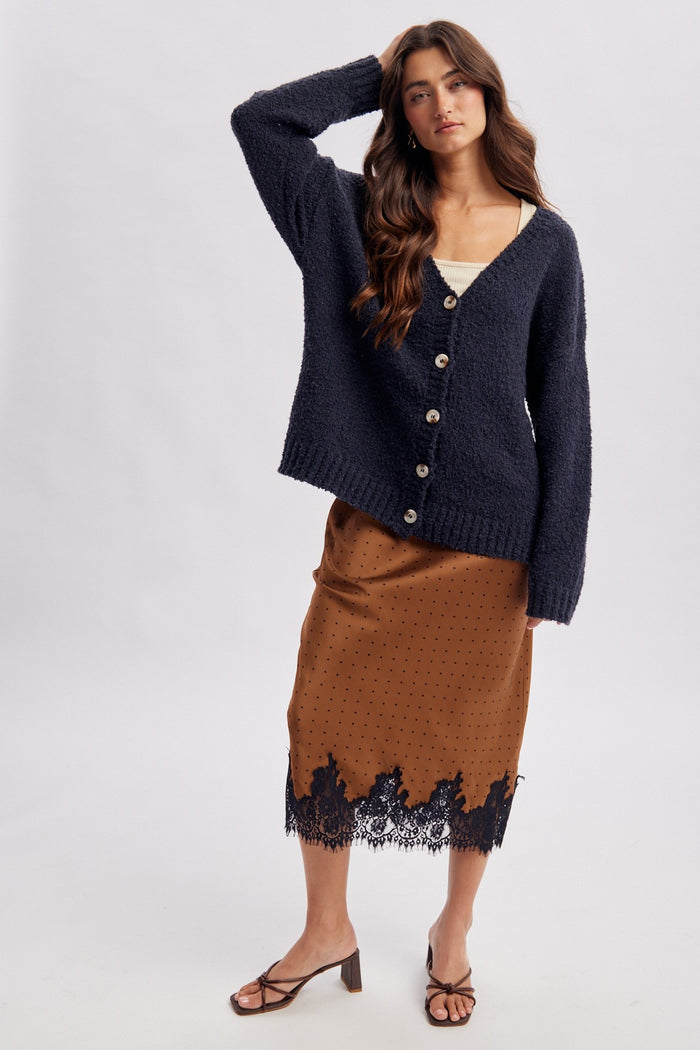 woman wearing a navy oversized cardigan over a cream top and a brown skirt with black lace detailing