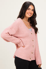 woman wearing a soft pink knitted cardigan with large buttons, styled casually with black pants and a gray top underneath