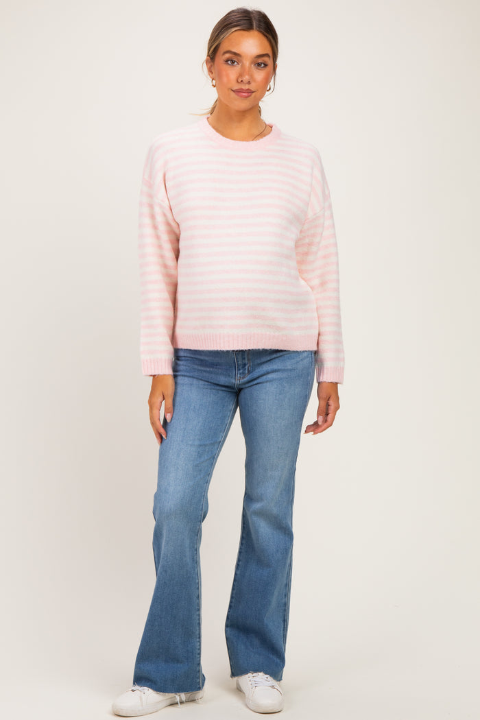 woman wearing a light pink striped maternity sweater and blue flared jeans, with a relaxed fit