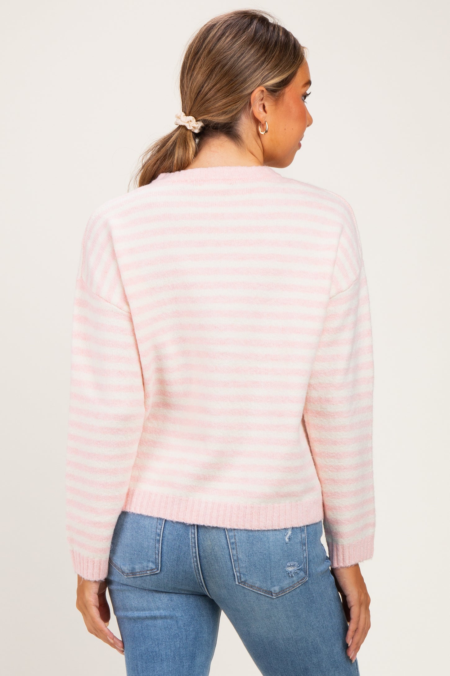 woman wearing a pink and white striped maternity sweater, showing her back, paired with blue jeans