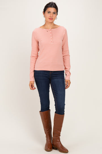 woman wearing a pink and white striped long sleeve henley top with button details and blue skinny jeans, standing in tall brown boots