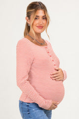 woman wearing a coral and white striped maternity top, holding her baby bump and smiling