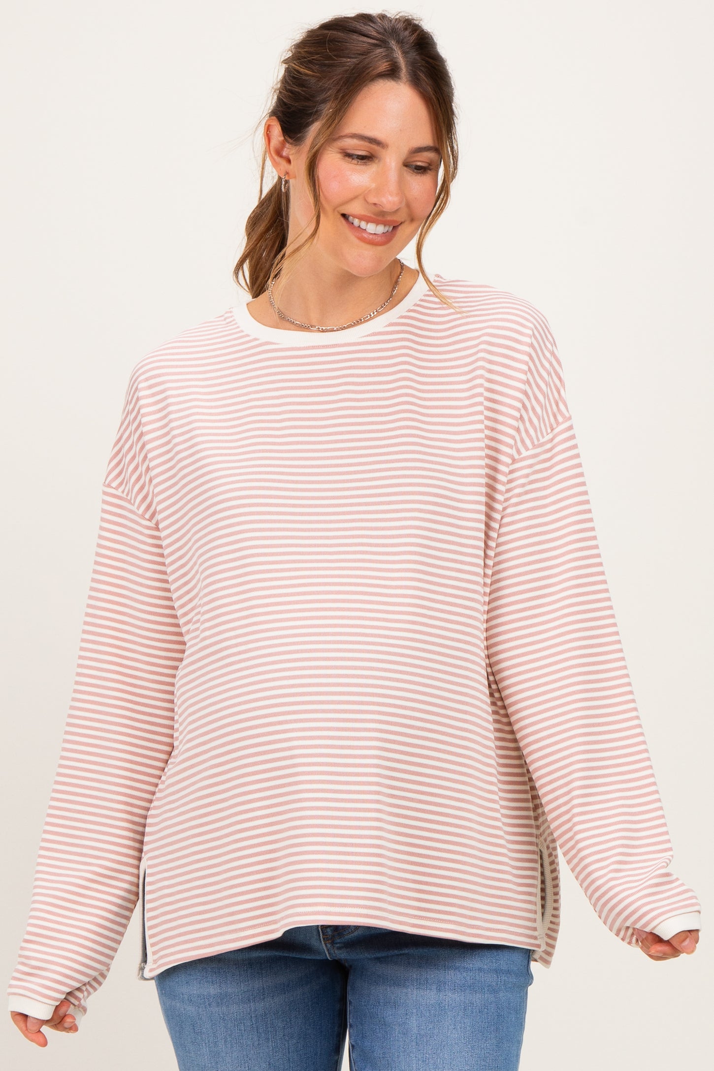 woman wearing a light pink and white striped maternity top with relaxed fit and side slits, smiling at the camera