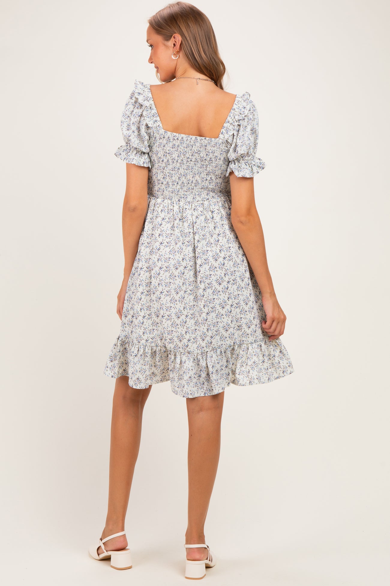 woman wearing a floral print maternity dress with short puff sleeves and a ruffled hem, showing a baby bump