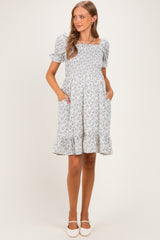 woman wearing a light blue floral maternity dress with puff sleeves and a ruffled hem, featuring pockets