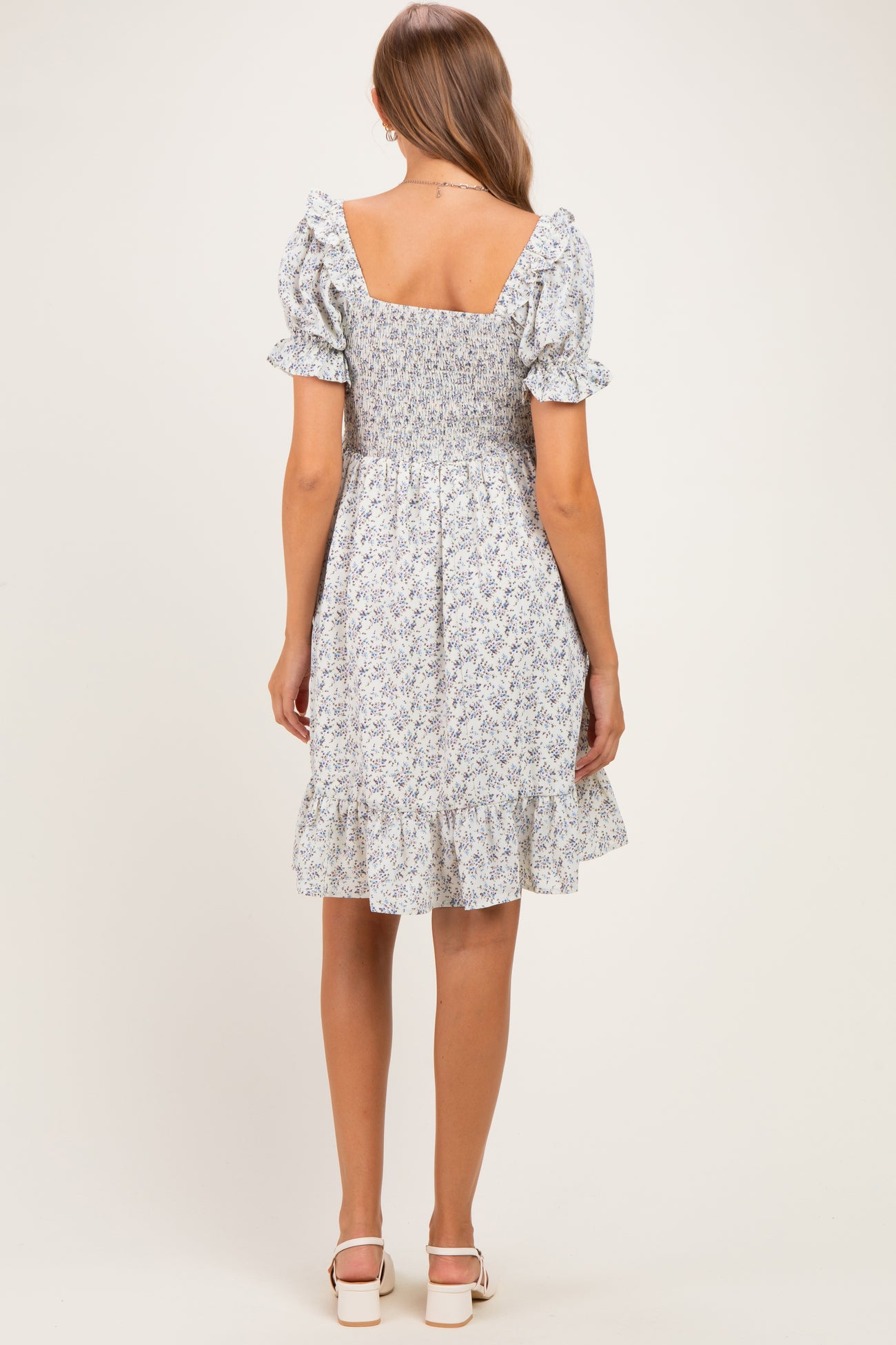 woman wearing a floral print maternity dress with puff sleeves and a ruffled hem, showing the back view