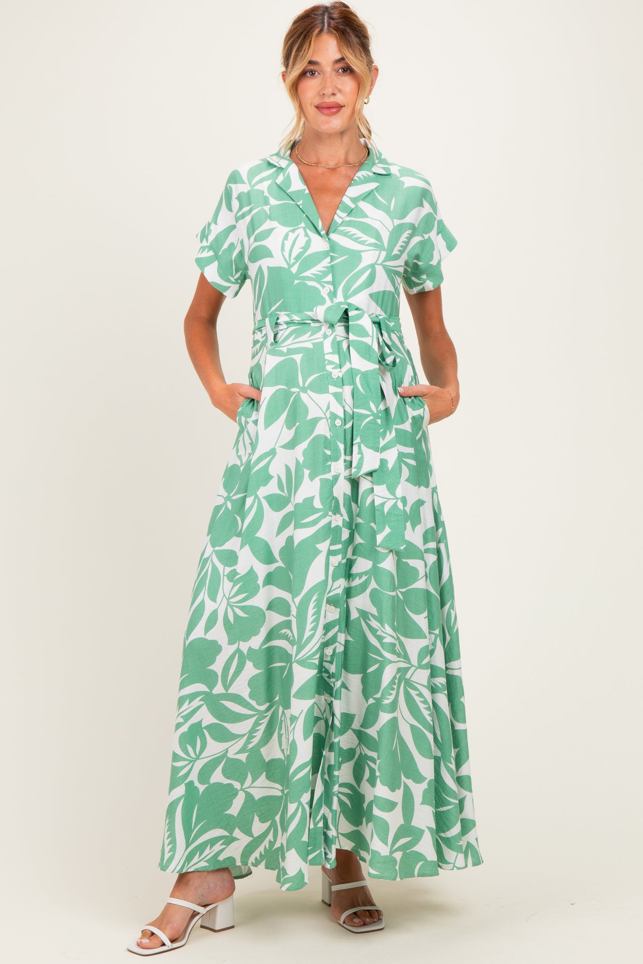 woman wearing a green and white floral maternity maxi dress with short sleeves and a tie waist, pockets visible