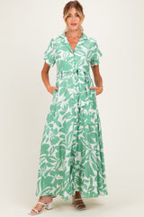 woman wearing a green and white floral maternity maxi dress with short sleeves and a tie waist, pockets visible