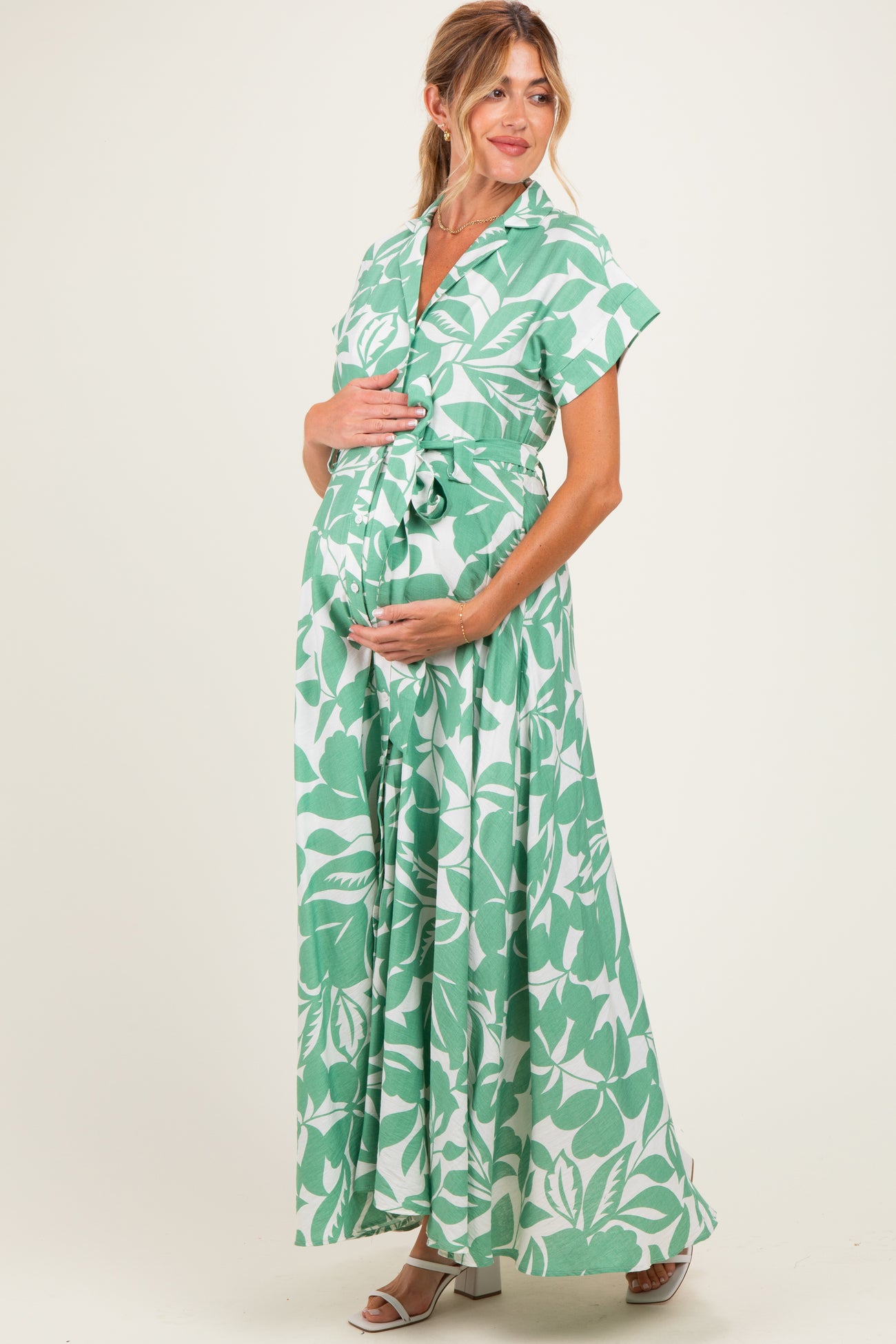 woman wearing a green and white floral maternity maxi dress and posing with her baby bump