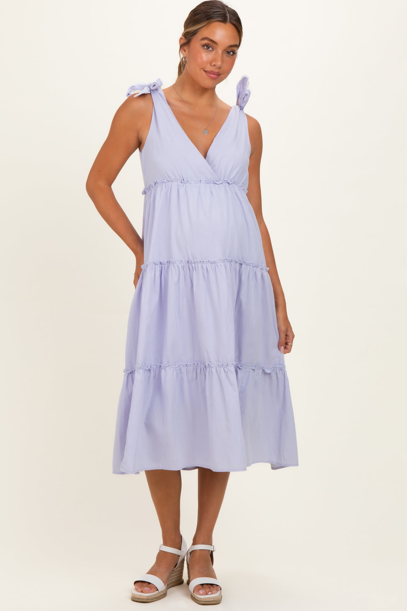 woman wearing a lavender maternity dress with tie shoulder straps and tiered ruffle details, showcasing her baby bump