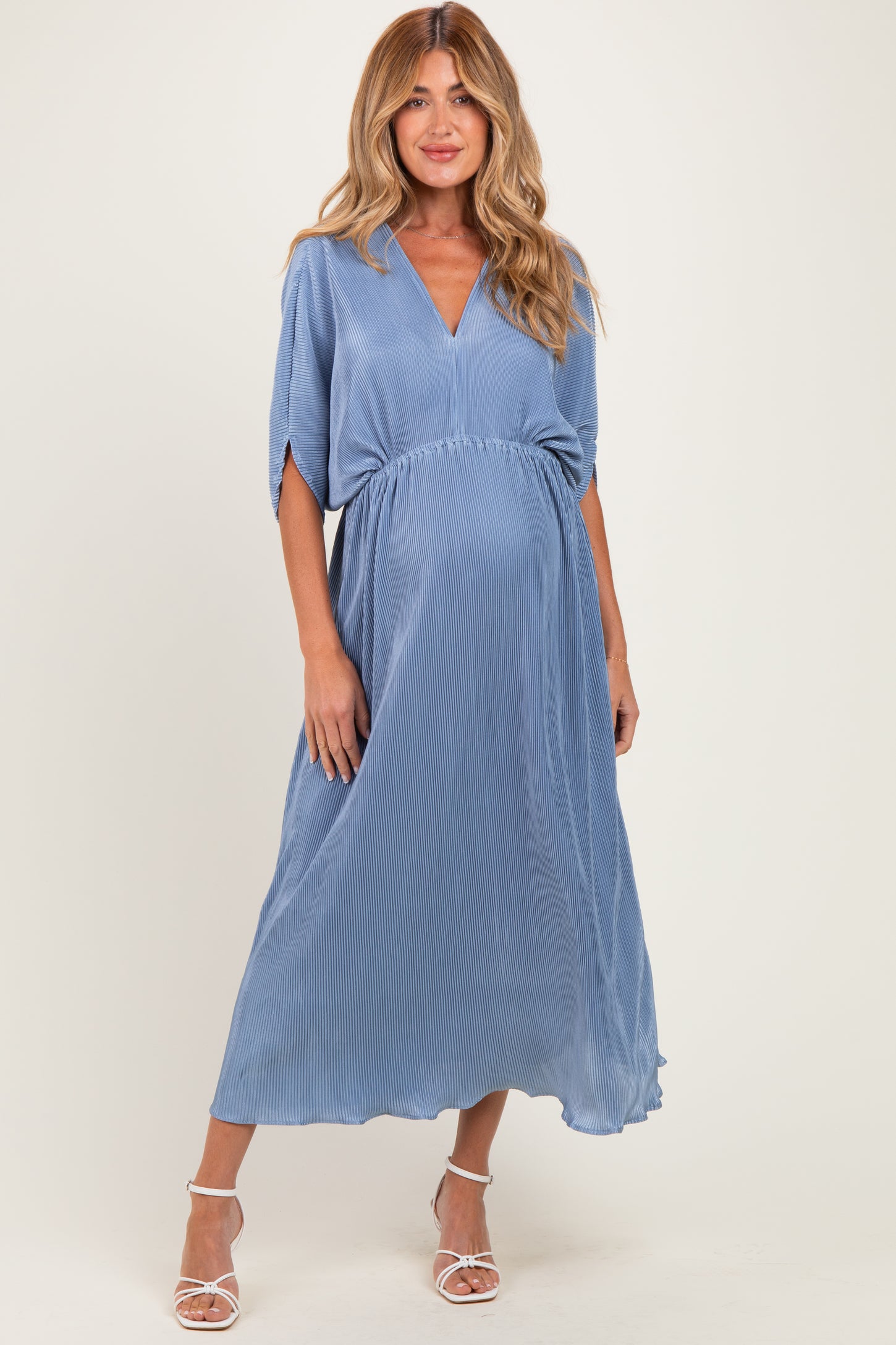 woman wearing a blue pleated maternity dress with a v-neckline and short sleeves, showcasing her baby bump