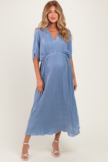 woman wearing a blue pleated maternity dress with a v-neckline and short sleeves, showcasing her baby bump