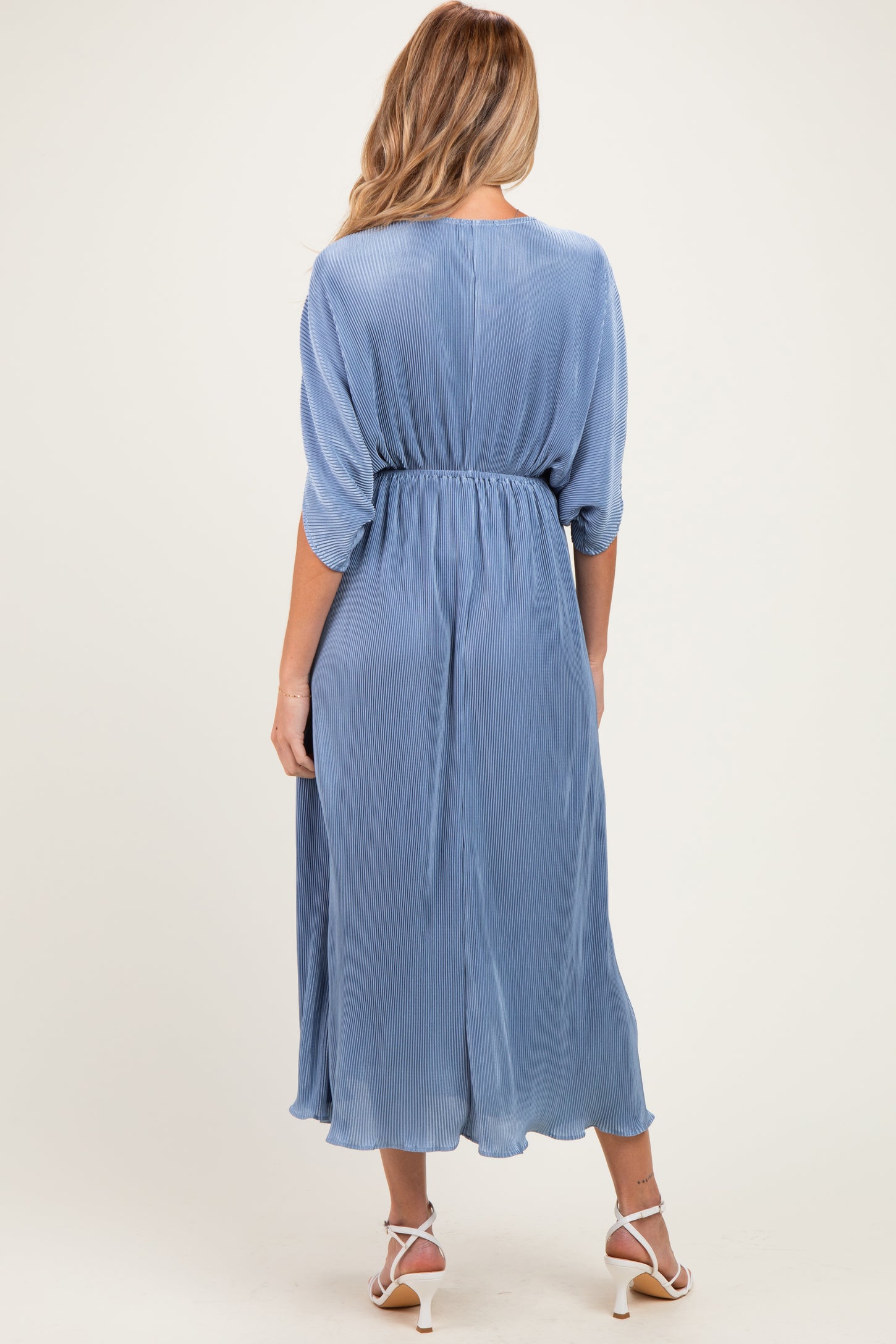 woman wearing a light blue pleated maternity dress with a cinched waist and three-quarter sleeves, showing her baby bump