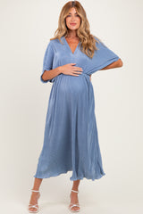 woman wearing a blue pleated maternity dress with a v-neck and flowing sleeves, holding her baby bump