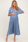 woman wearing a blue pleated maternity dress with a v-neck and flowing sleeves, holding her baby bump