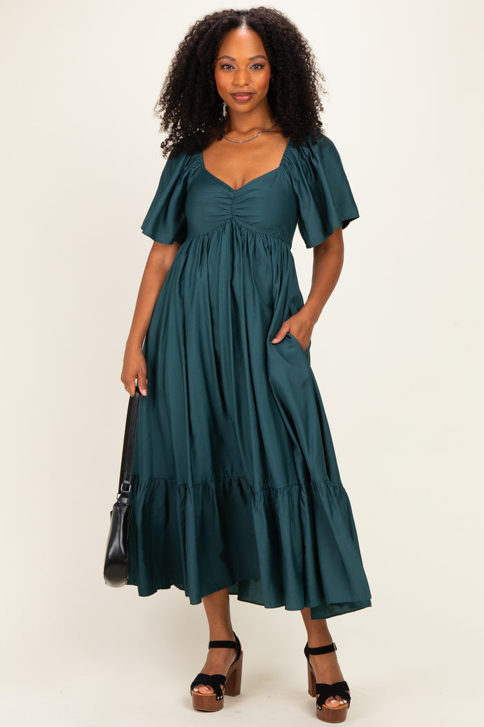 woman wearing a dark green midi dress with puff sleeves and a tiered skirt, holding a black handbag