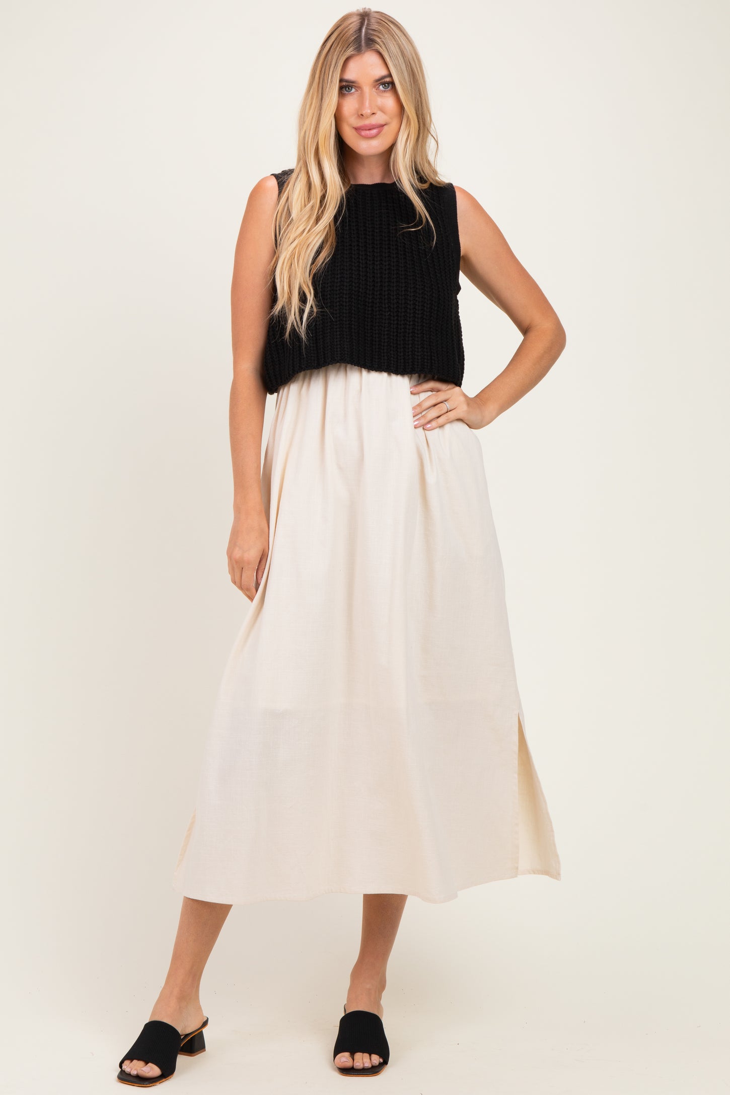 woman wearing a black knitted crop top over a cream maxi dress with side slits and black slide sandals