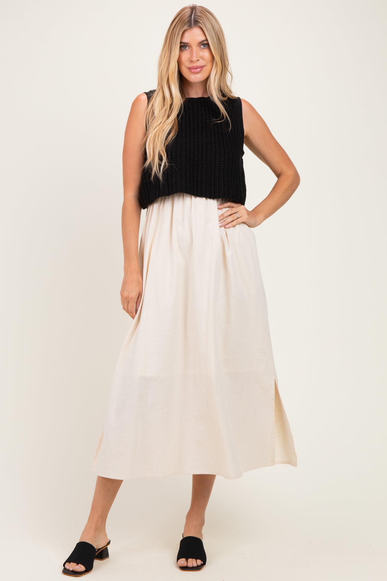 woman wearing a black knitted crop top over a cream maxi dress with side slits and black slide sandals