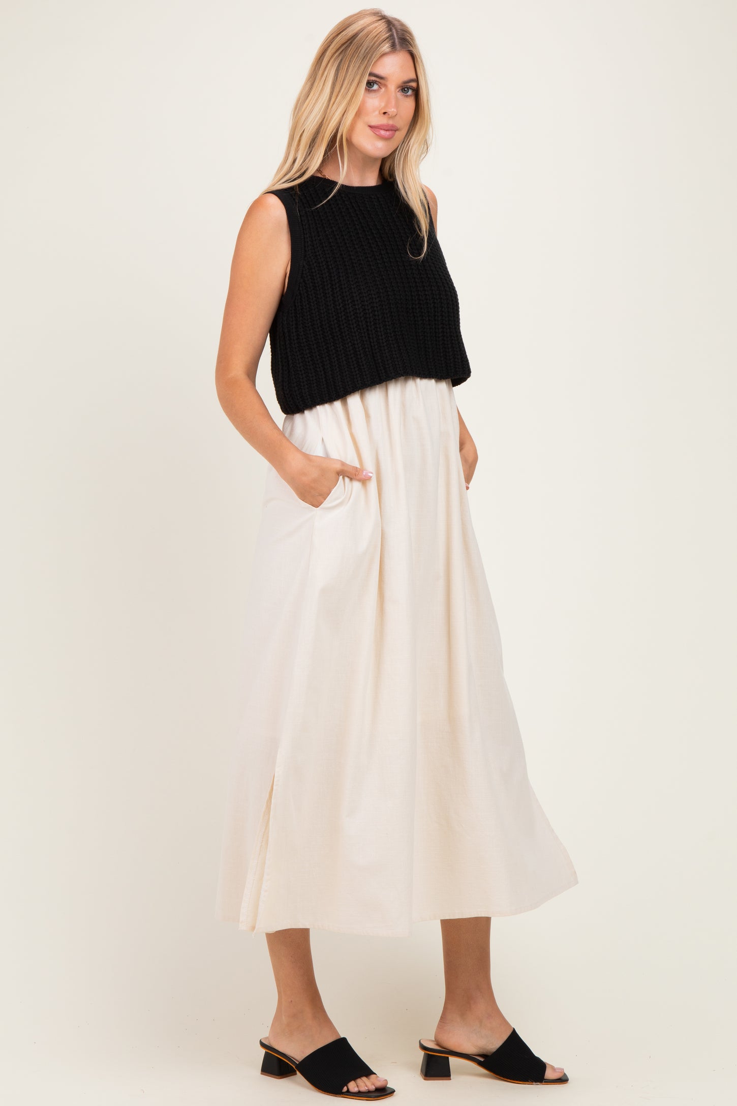 woman wearing a black cropped sweater over a cream-colored maxi dress with side pockets and side slits