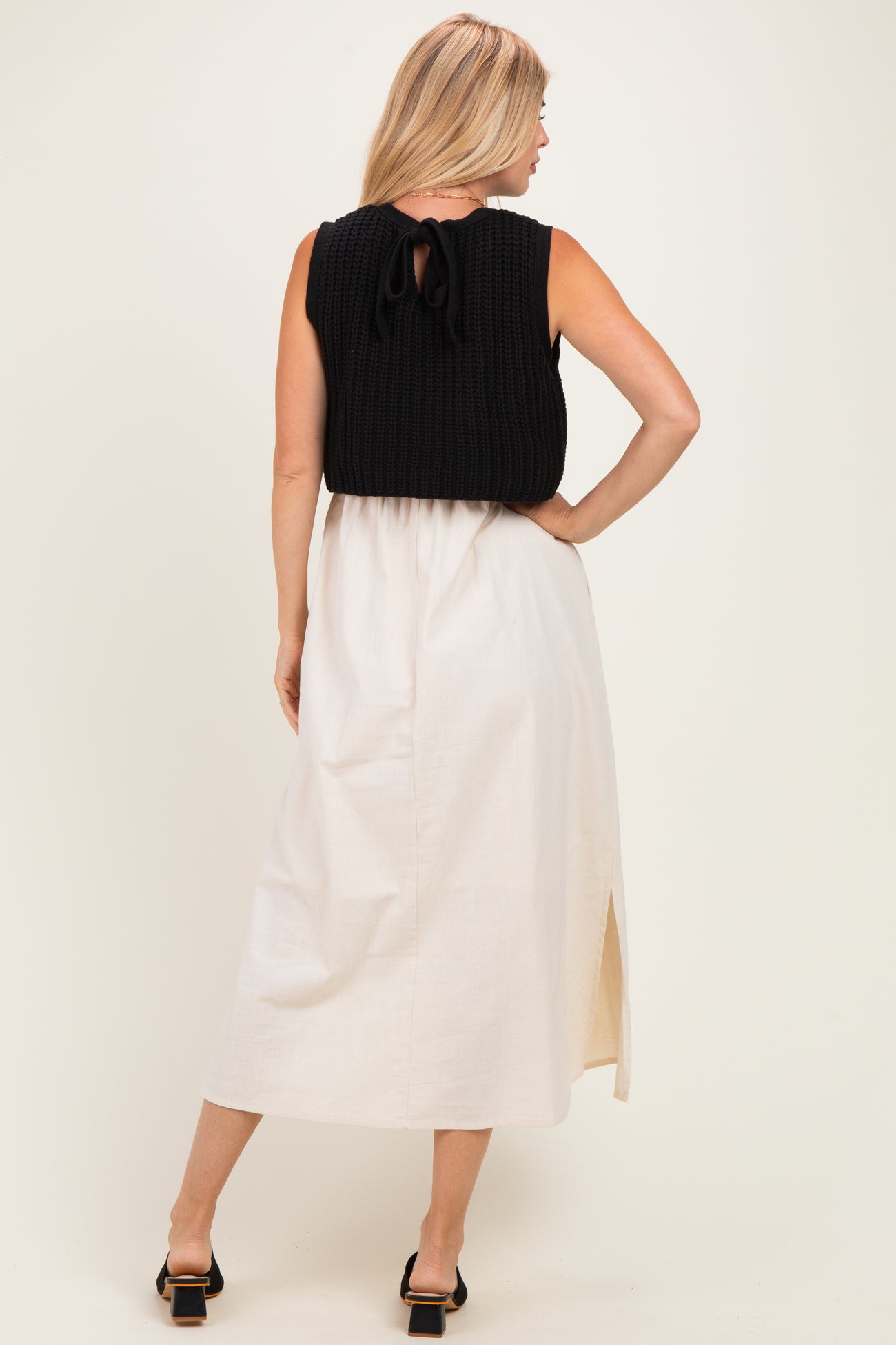 woman wearing a black knitted sleeveless top with a tie-back detail and a white maxi skirt with a side slit