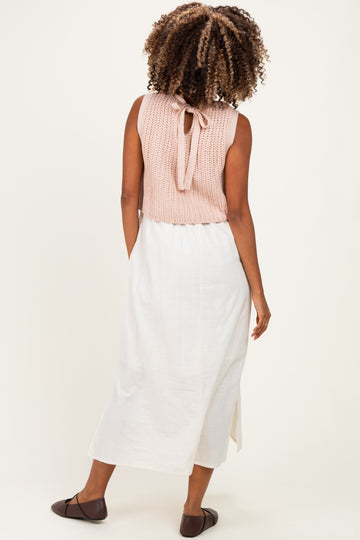 woman wearing a light pink sleeveless maternity top with a back tie, paired with a white maxi skirt