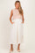 woman wearing a knitted blush maternity crop top over a white maxi dress with pockets and a side slit