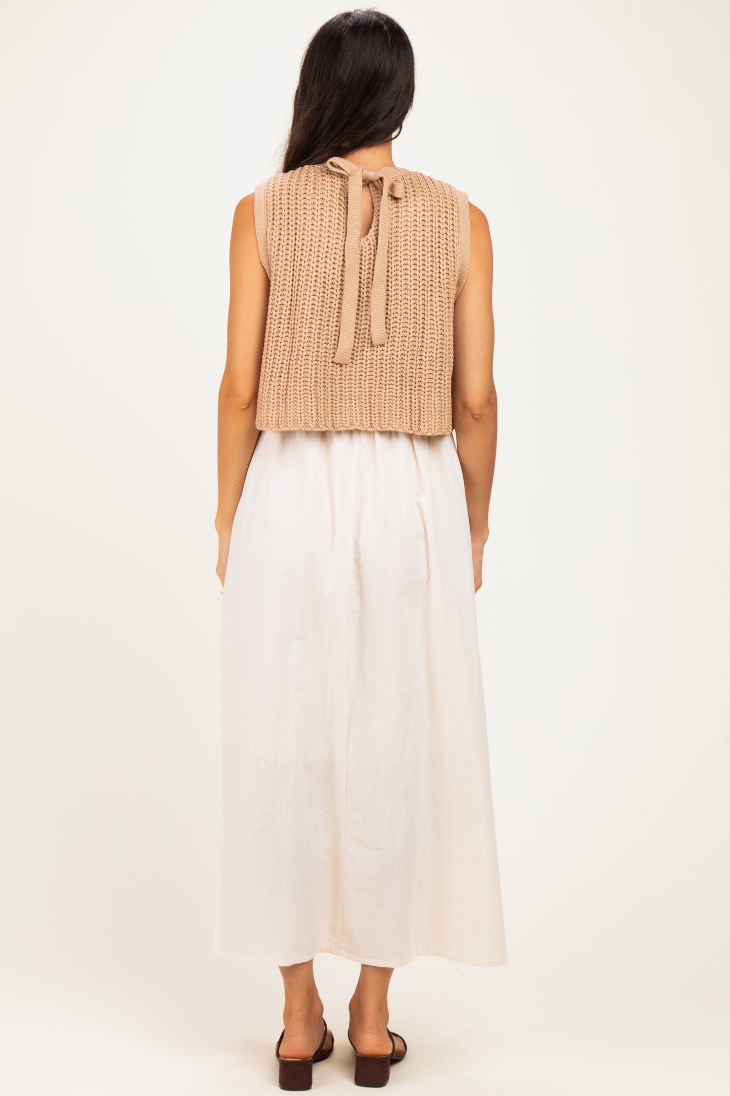 woman wearing a beige knitted sleeveless top with ties, paired with a flowy white maxi dress