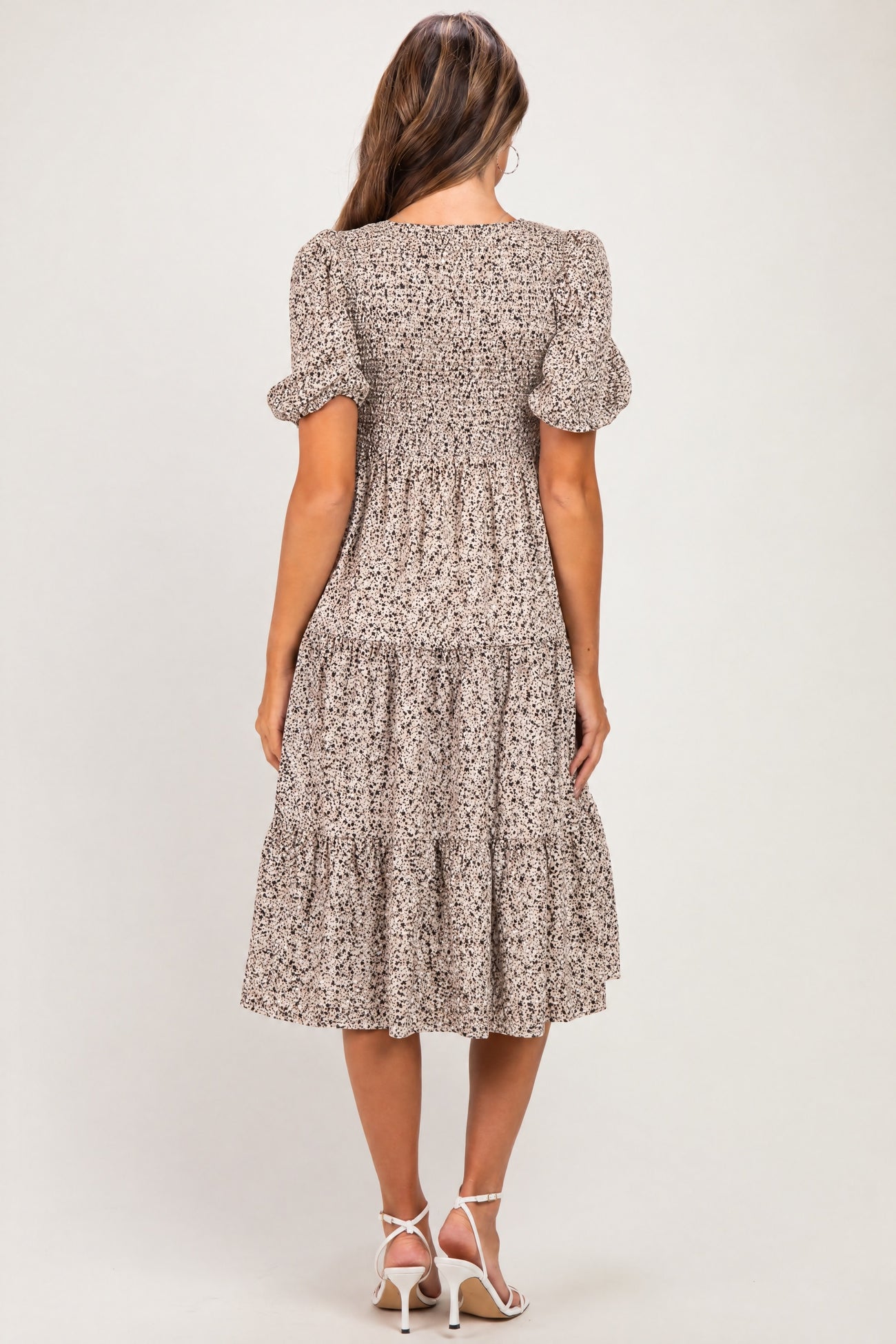 woman wearing a floral print maternity dress with puff sleeves and a tiered hem, showing her baby bump from the back