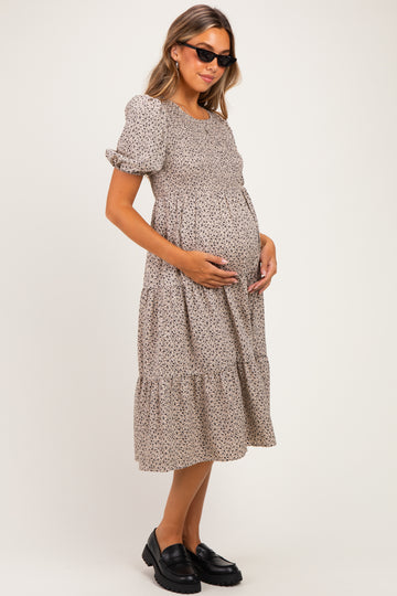 woman wearing a brown floral maternity dress with puff sleeves and a baby bump, accessorized with sunglasses and black shoes