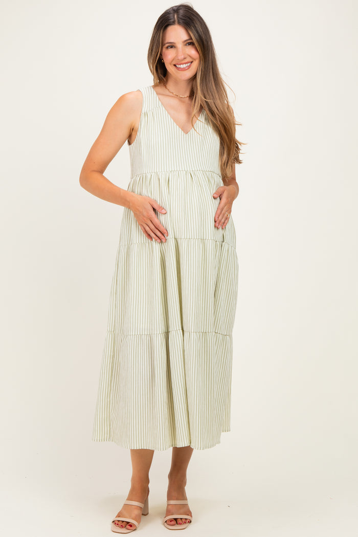 woman wearing a light green and white striped maternity dress, standing and cradling her baby bump