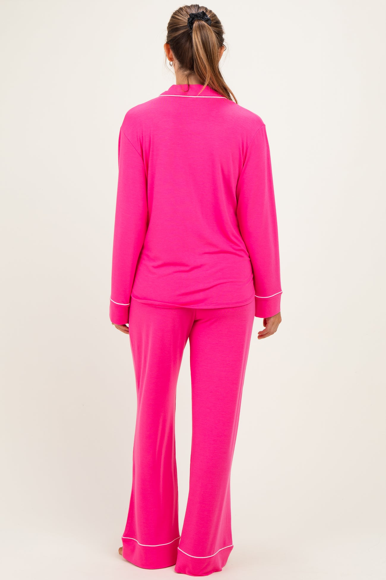 woman wearing a bright pink maternity pajama set with long sleeves and flared pants, view from the back