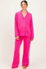 woman wearing a bright pink maternity pajama set with long sleeves and pants, featuring white piping details and a visible baby bump