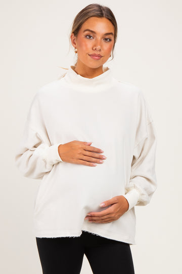 woman wearing a cream maternity oversized sweatshirt and holding her baby bump