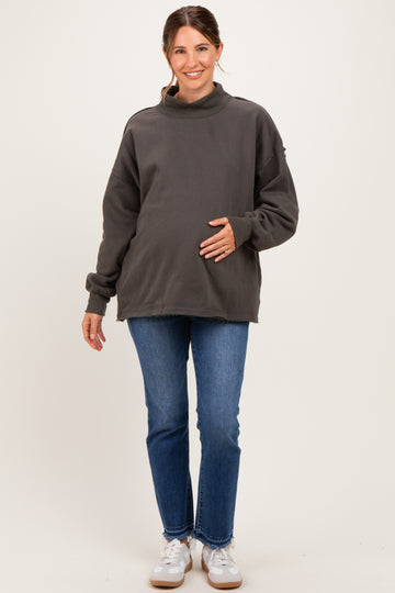woman wearing a dark gray maternity sweatshirt and blue jeans, holding her baby bump