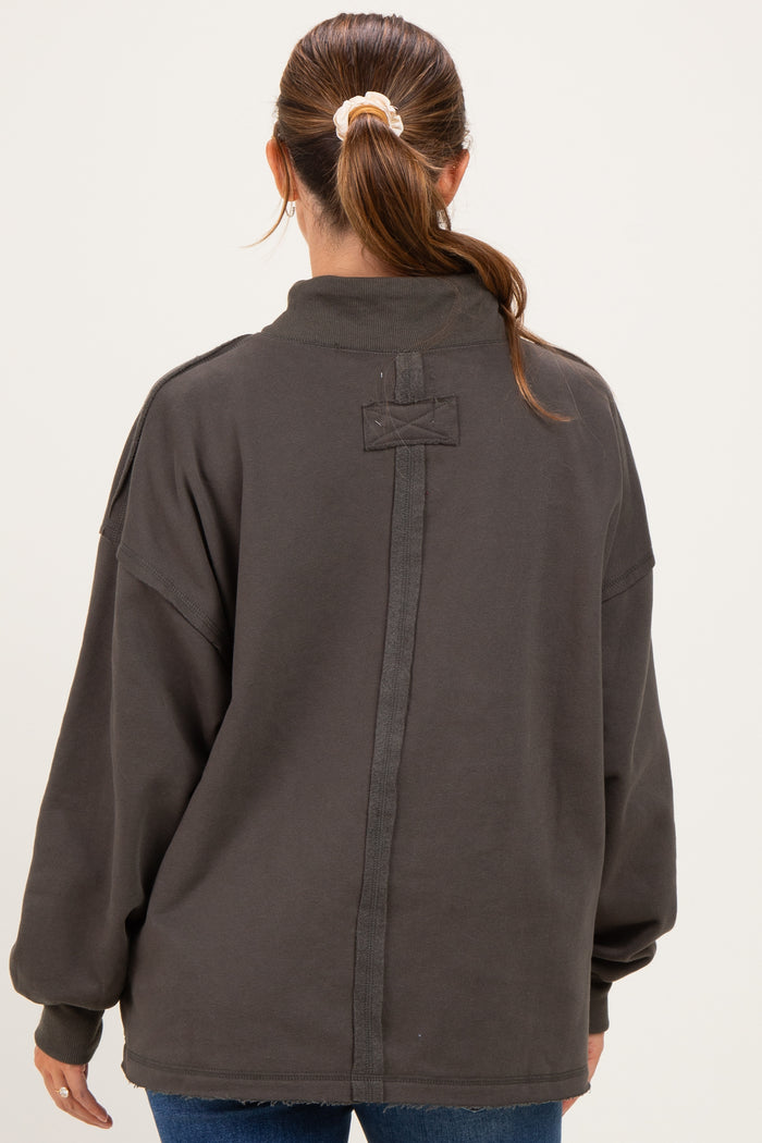 woman wearing a dark gray oversized maternity sweatshirt with a high collar and seam detail on the back