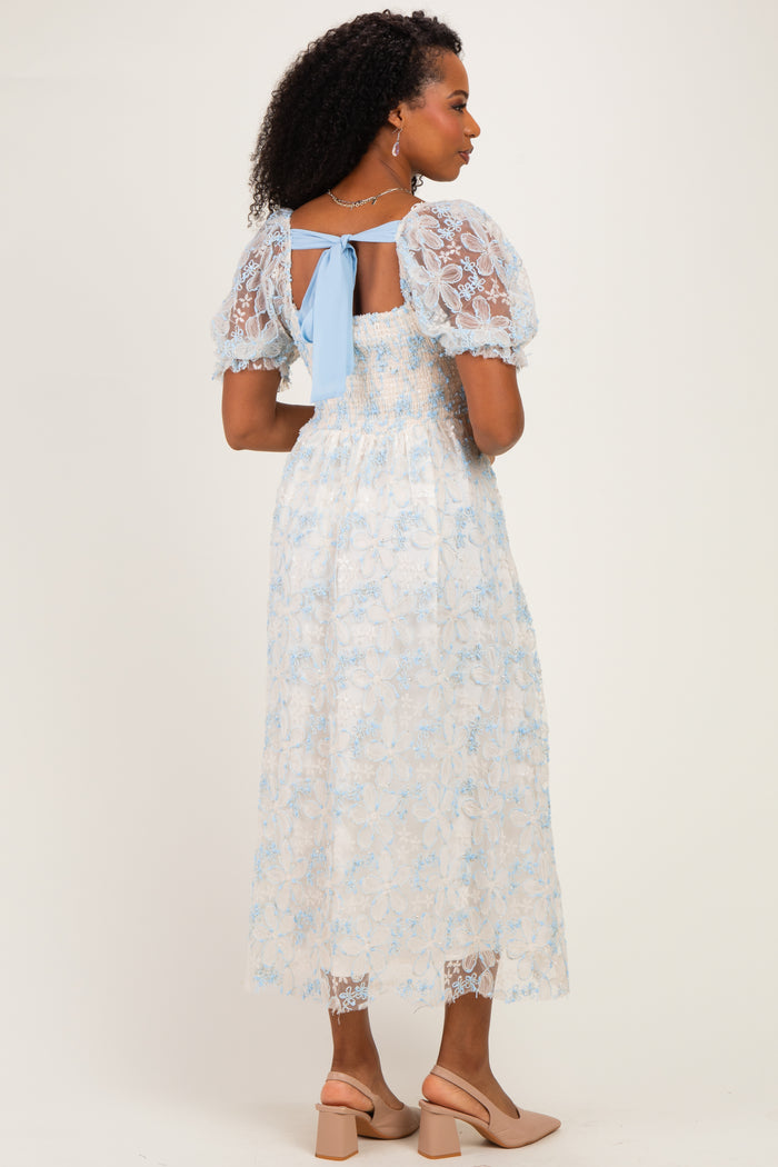 woman wearing a light blue floral lace midi dress with puff sleeves and a back tie detail