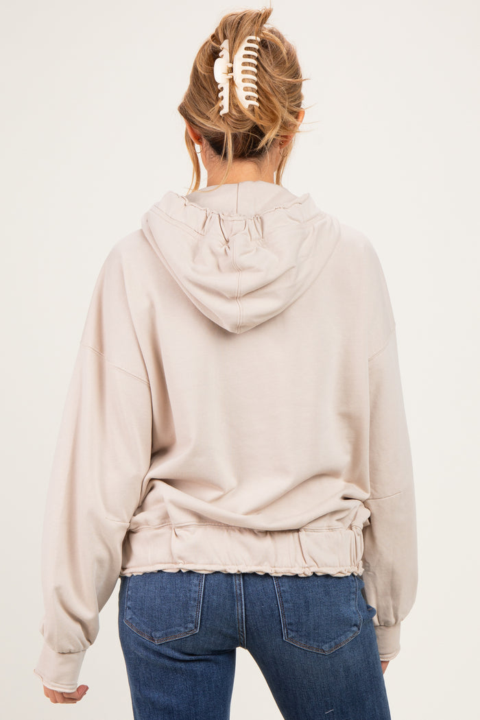 woman wearing a beige maternity hoodie with a cinched waist and hood, seen from the back