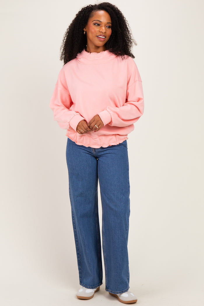 woman wearing a pink oversized sweatshirt with ruffle detailing and high-waisted blue wide-leg jeans