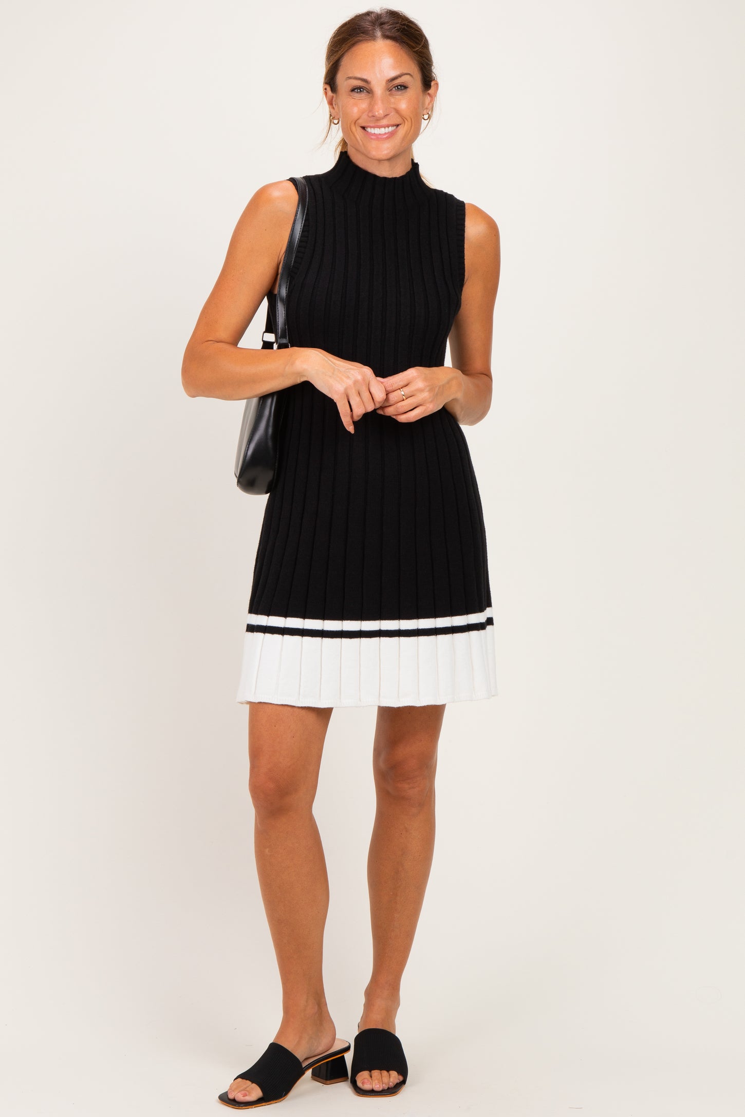 woman wearing a black sleeveless ribbed knit dress with a white pleated hem and carrying a black handbag