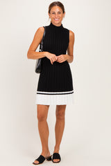 woman wearing a black sleeveless ribbed knit dress with a white pleated hem and carrying a black handbag