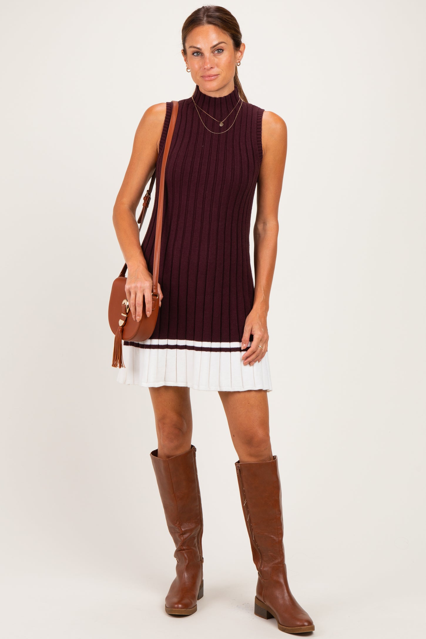 woman wearing a maroon sleeveless ribbed sweater dress with a white ruffled hem and brown knee-high boots.