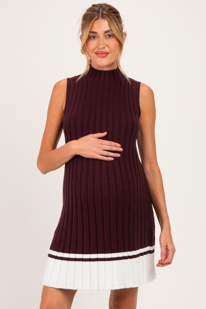 woman wearing a burgundy ribbed maternity dress with a sleeveless design and pleated white skirt, showing her baby bump