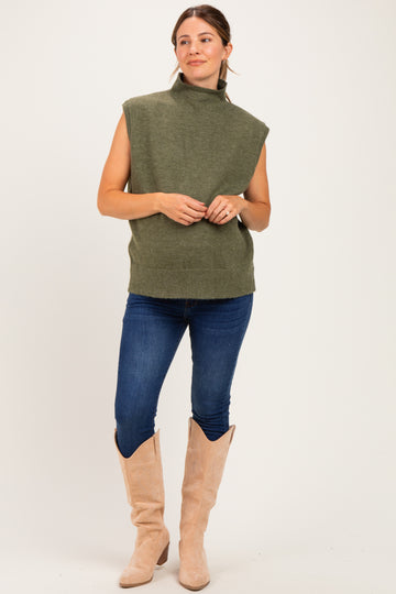 woman wearing a green sleeveless turtleneck sweater and blue jeans, styled for maternity wear