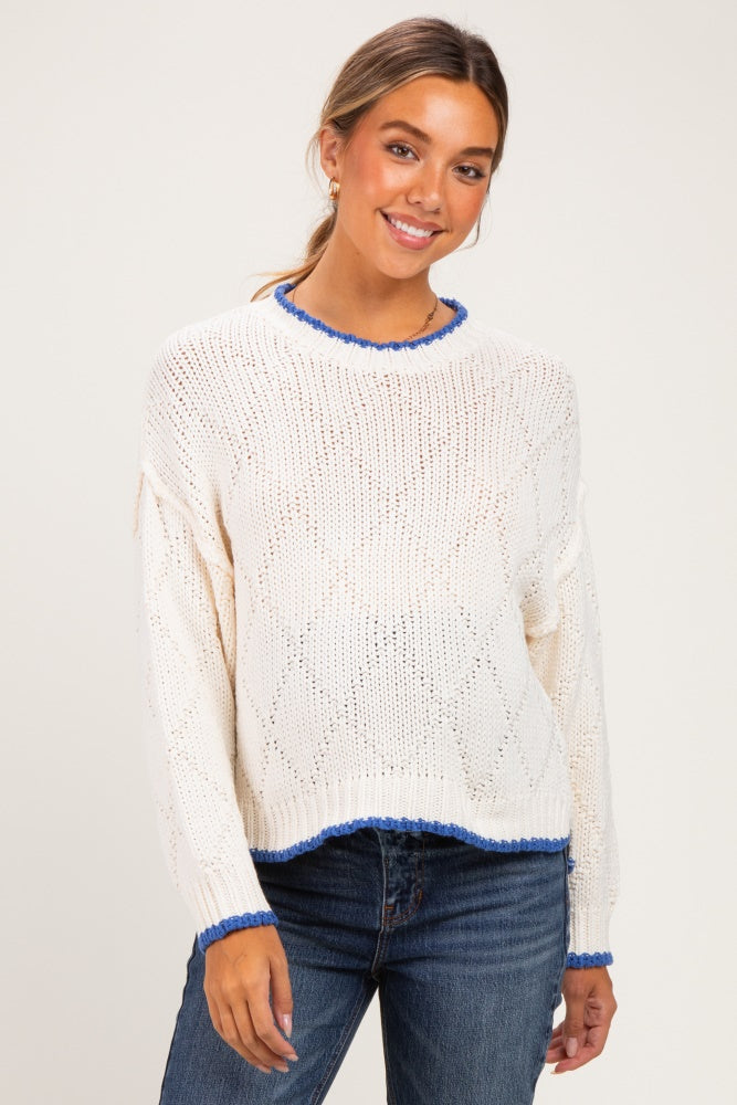 woman wearing a white knit maternity sweater with blue trim and a relaxed fit, smiling at the camera