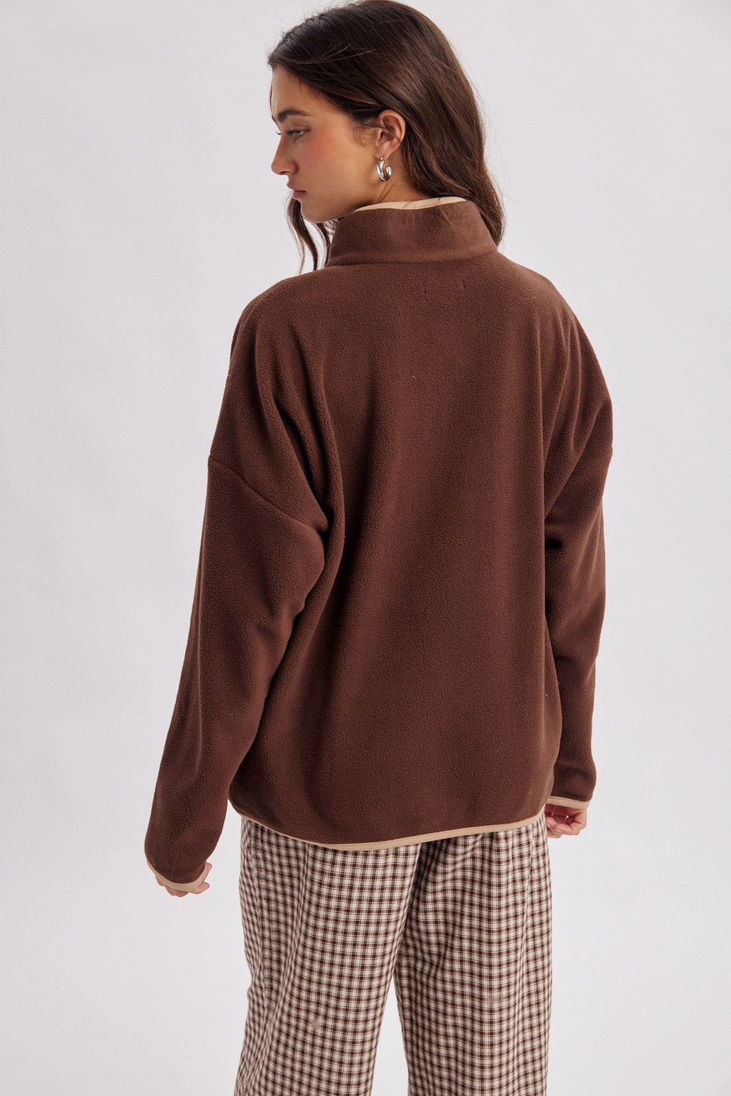 woman wearing a brown fleece pullover with a high collar and oversized fit, paired with checkered trousers