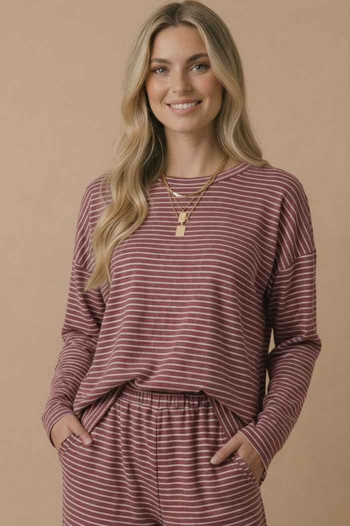 woman wearing a maroon and white striped long sleeve top with pockets and matching bottoms, smiling at the camera